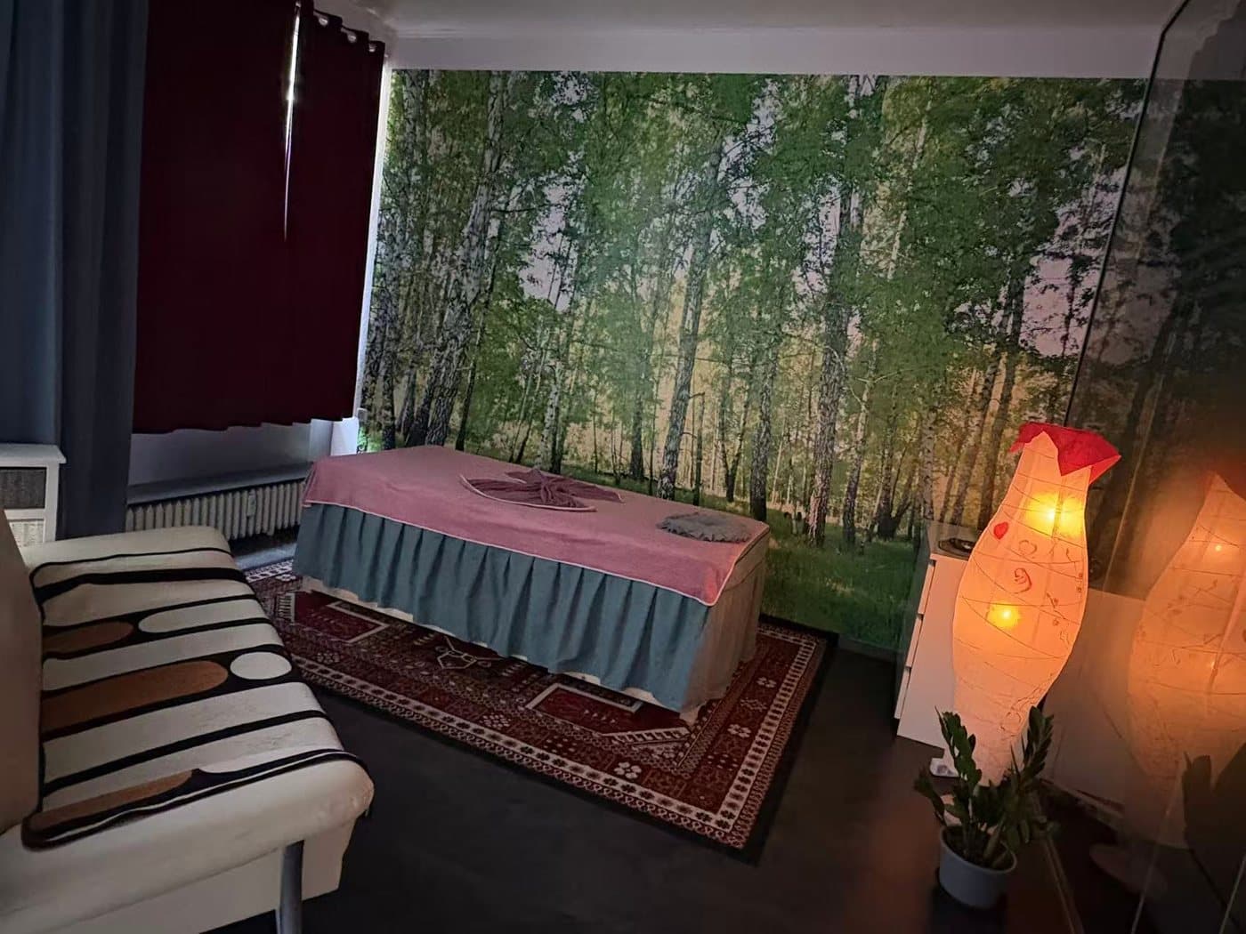 Behandlungsraum bei Shufu Massage mit Waldmotiv an der Wand und stimmungsvollen Lampen